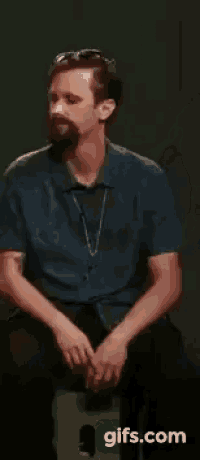 a man with a beard is sitting on a stool with his hands folded .