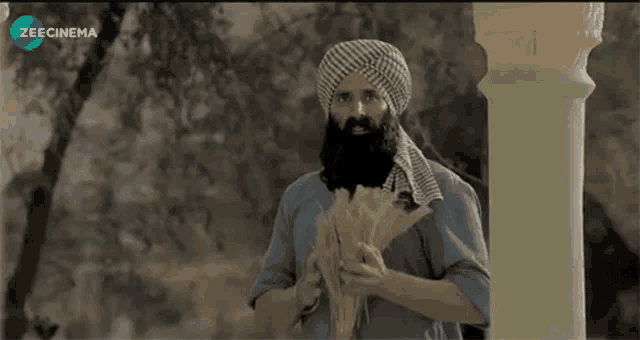 a man with a beard is holding a bunch of wheat in front of a screen that says zee cinema