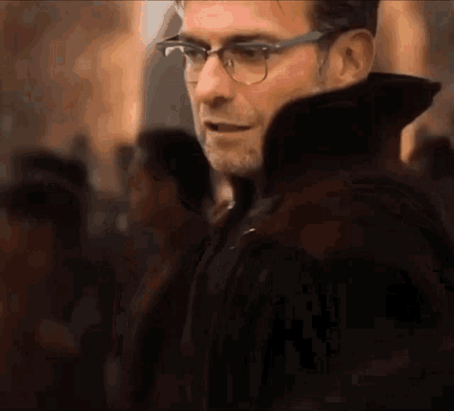 a man wearing glasses and a black coat is standing in a crowd