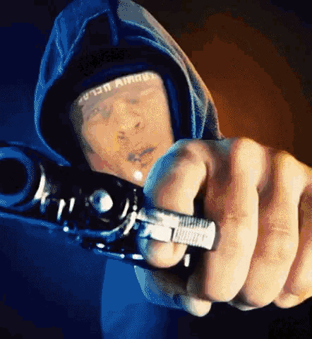 a man in a hoodie holds a gun in front of his face with a bandage that says ' against ' on it