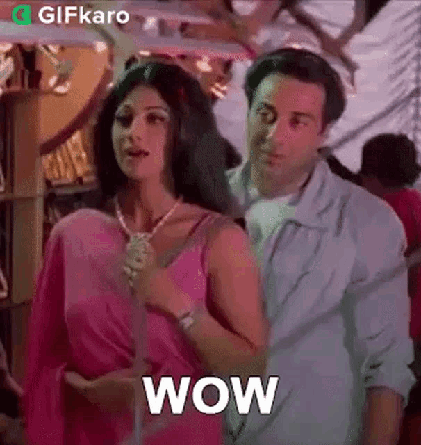 a man and a woman are standing next to each other and the woman is wearing a pink saree and necklace .