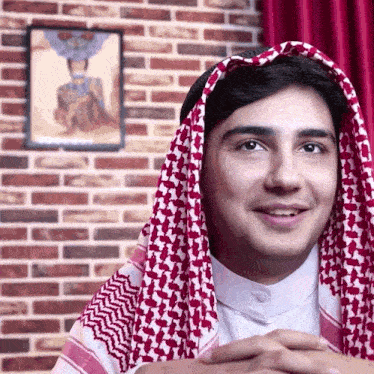 a man wearing a red and white scarf around his head smiles in front of a brick wall
