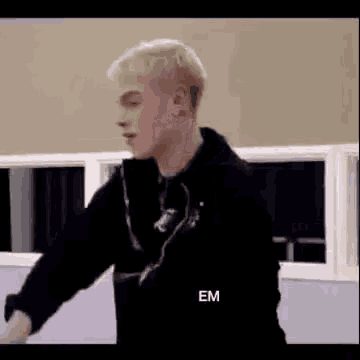 a man with blonde hair is standing in front of a window in a room .