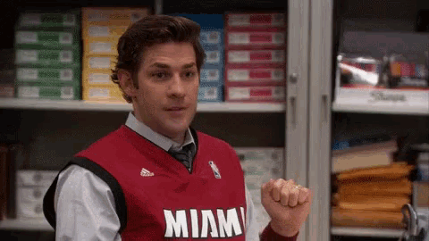 a man wearing a red miami jersey is standing in front of a shelf full of binders .