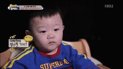 a baby is sitting in a chair wearing a blue shirt that says super dad .