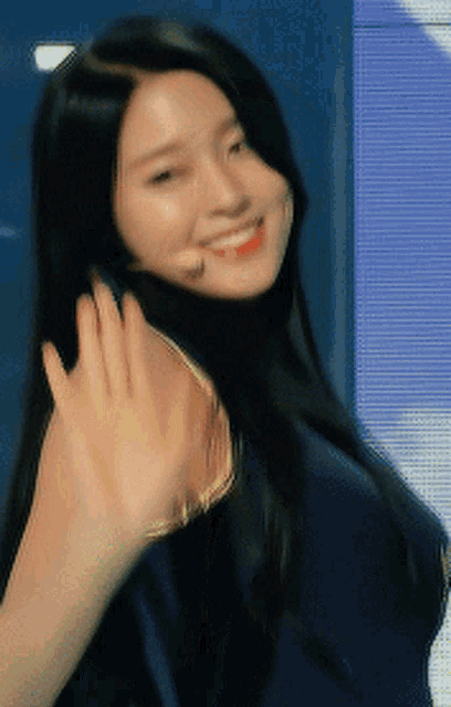 a woman with long black hair is waving her hand