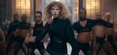 a woman in a black dress is dancing in front of a group of men in black shirts .
