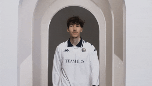 a man in a white team bds shirt stands in an archway