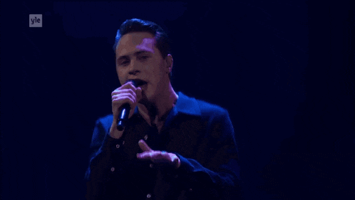 a young man singing into a microphone with the letters yle behind him