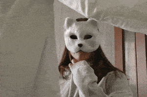 a woman in a grey sweatshirt is holding a piece of paper over her head