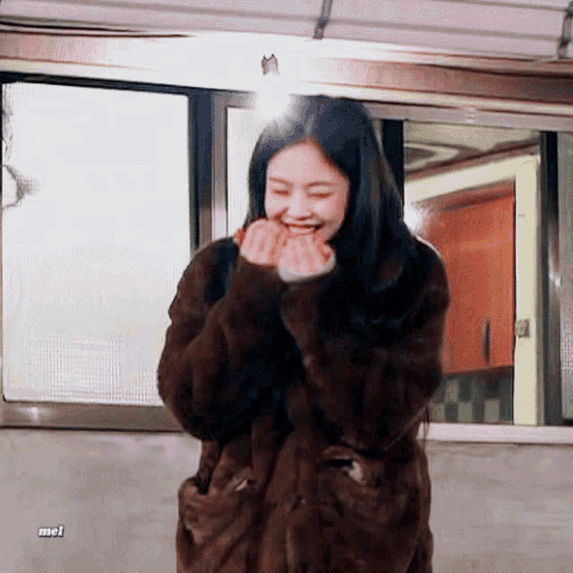 a woman wearing a fur coat is smiling in front of a window with mel written on the bottom right corner