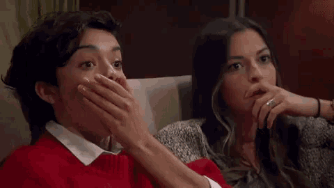 a woman is covering her mouth with her hand while sitting on a couch next to another woman .