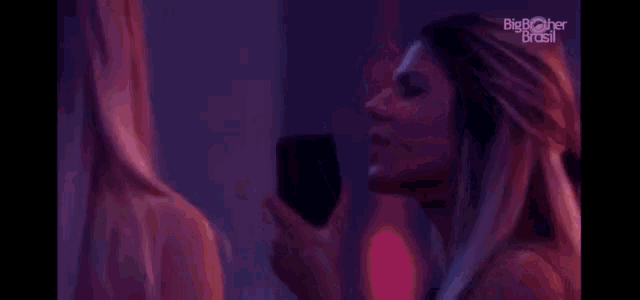 two women are kissing each other in a dark room with purple lights .