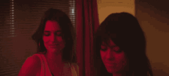 two women are standing next to each other in front of a window with blinds .