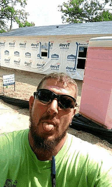 a man wearing sunglasses takes a selfie in front of a house with a sign that says ' i love you '