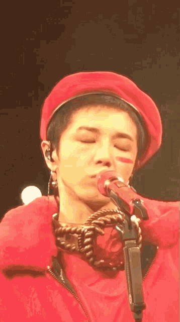 a man wearing a red hat is singing into a microphone with his eyes closed