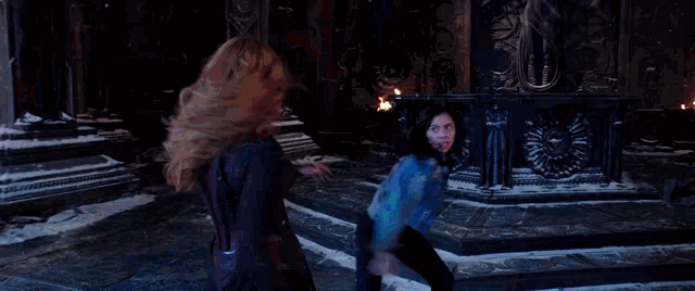 two women are fighting in a dark room with a blue light coming out of the ceiling .