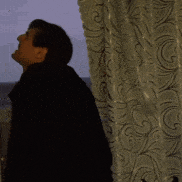 a man in a black jacket is standing in front of a window and making a funny face