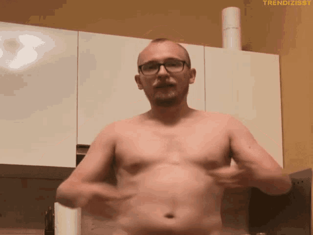 a shirtless man with glasses and a beard is standing in front of white cabinets with the hashtag trendizisst on the bottom