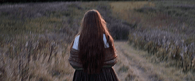 a woman with long hair is walking down a dirt road