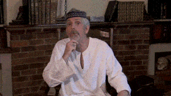a man in a white shirt and blue hat is sitting in front of a fireplace