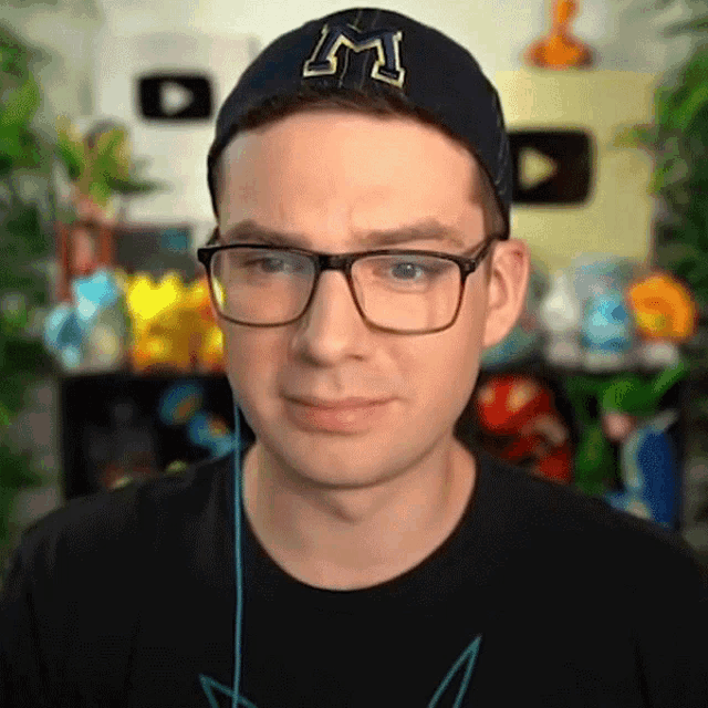 a man wearing glasses and a hat with the letter m on it is looking at the camera .