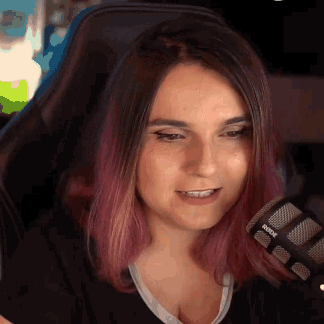 a woman with purple hair is sitting in front of a rode microphone .
