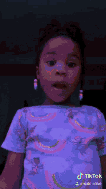 a little girl is wearing a purple shirt with a rainbow print and a tiktok watermark