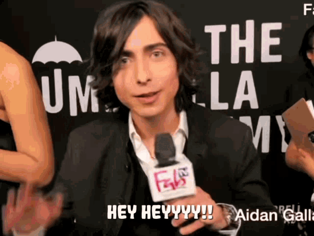 a man in a suit is holding a microphone and saying hey heyyy