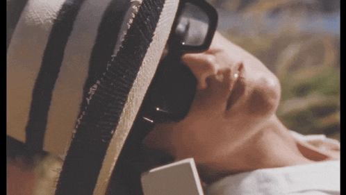 a woman wearing a straw hat and sunglasses is laying down