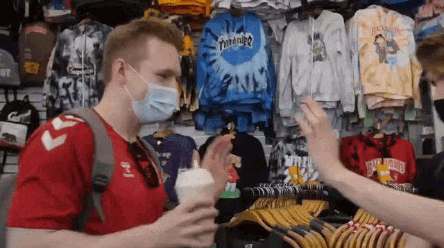 a man wearing a mask is giving a woman a high five in front of a wall of thrasher shirts