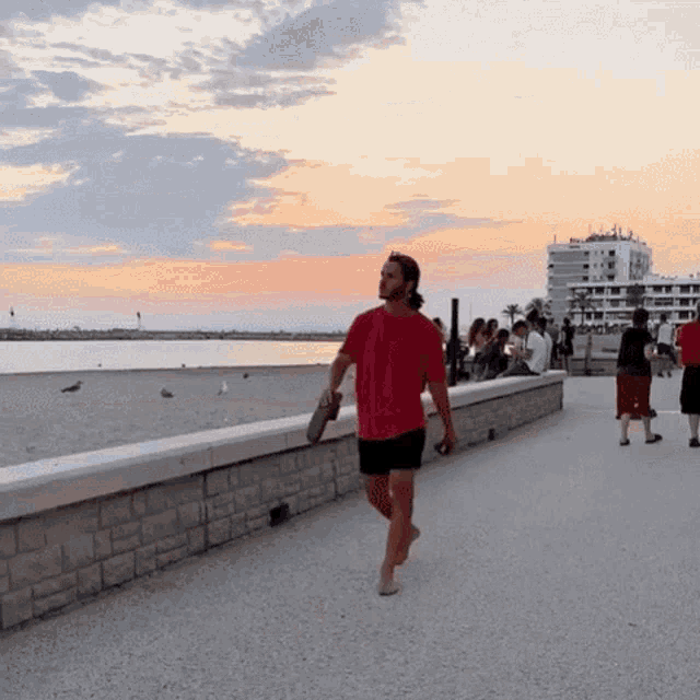 a man in a red shirt walks barefoot on a sidewalk near the beach
