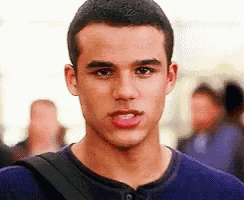a young man wearing a blue shirt and a black backpack is standing in a crowd .