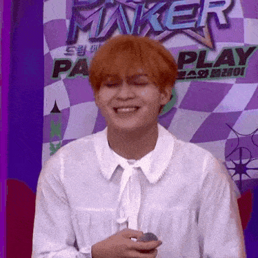 a man with red hair is holding a microphone in front of a purple and white checkered wall .