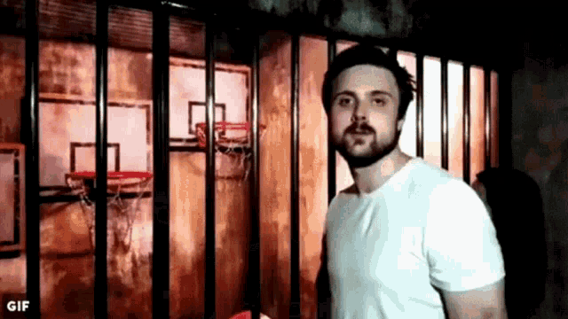 a man with a beard is standing in front of a basketball hoop behind bars .