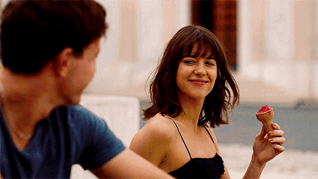 a woman in a black dress is holding an ice cream cone and smiling at a man