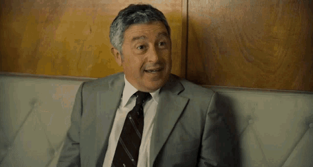 a man in a suit and tie is sitting on a couch with the words eccola la concorrenza written above him