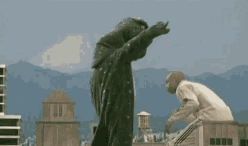 a man in a white sweater is standing in front of a giant monster .