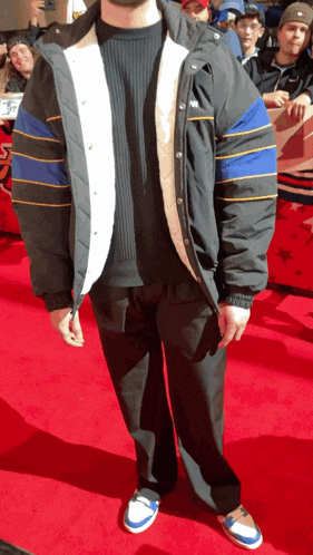a man is standing on a red carpet wearing a jacket