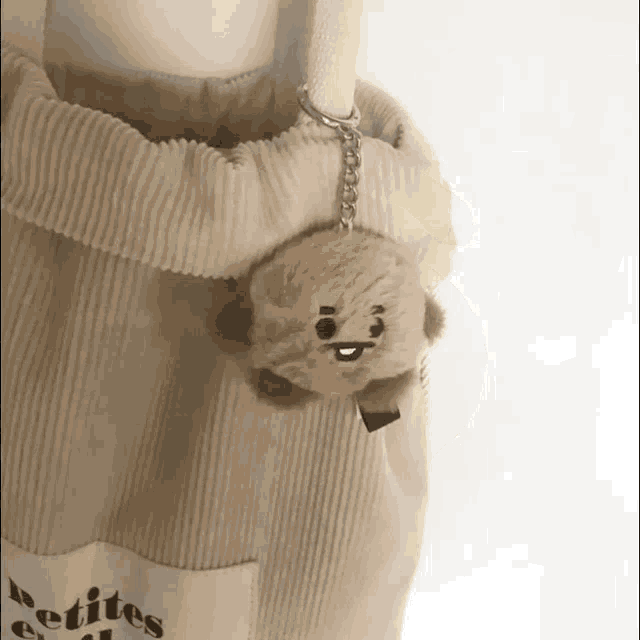 a small stuffed animal is hanging from the handle of a beige tote bag .