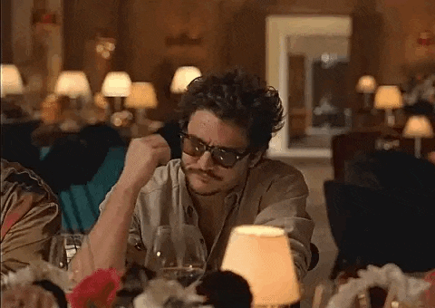 a man wearing sunglasses and a mustache is sitting at a table with a glass of wine .