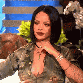 rihanna is sitting on a couch with her hand on her chin while wearing a military jacket .