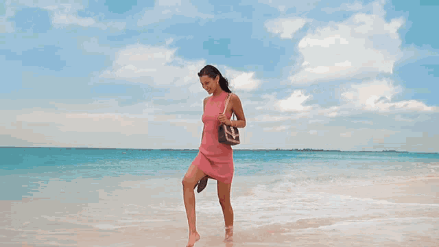 a woman in a pink dress is walking along the beach