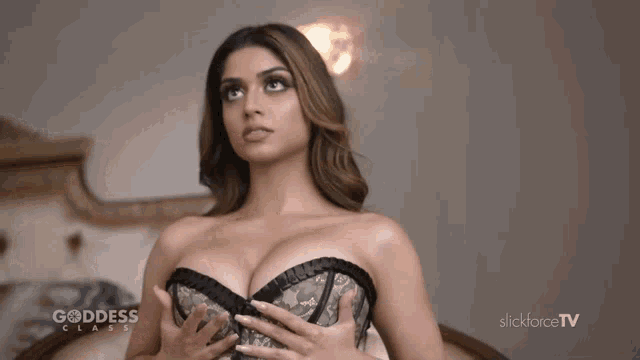 a woman in a corset is sitting on a bed in front of a slickforce tv ad