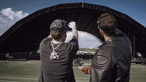 two men are standing in front of a large structure and one has a necklace with the letter t