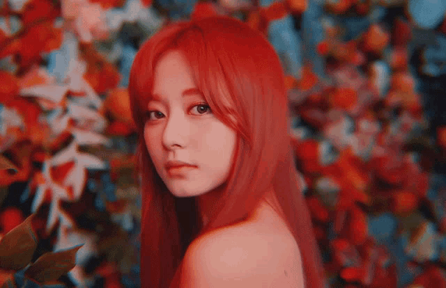 a woman with red hair is standing in front of a blurred background of flowers