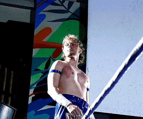 a man without a shirt is standing in a boxing ring holding a rope