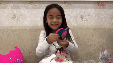 a little girl is sitting on a couch holding a stuffed animal in her hands .