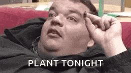 a fat man is laying on a couch holding a small object in his hand and says `` plant tonight '' .