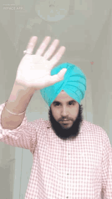 a man with a beard wearing a turban and a plaid shirt is waving his hand .